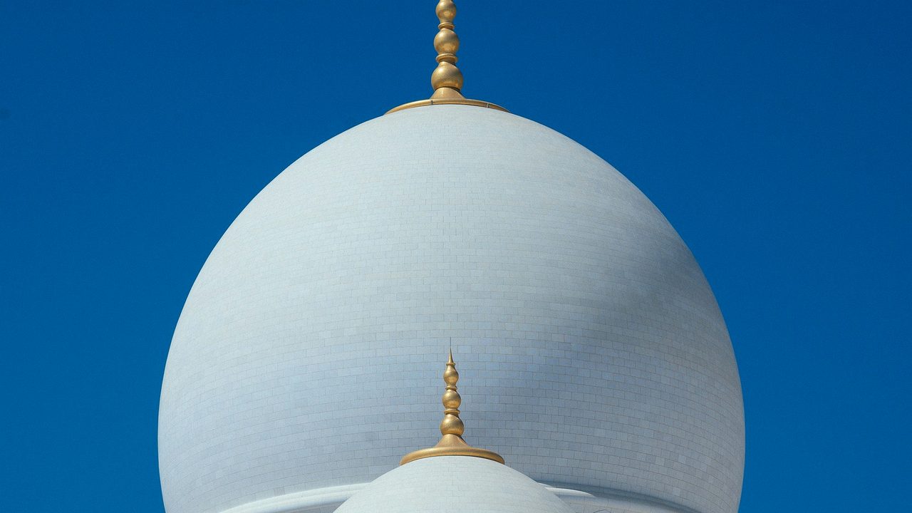 The white domes of a grand mosque against a clear blue sky