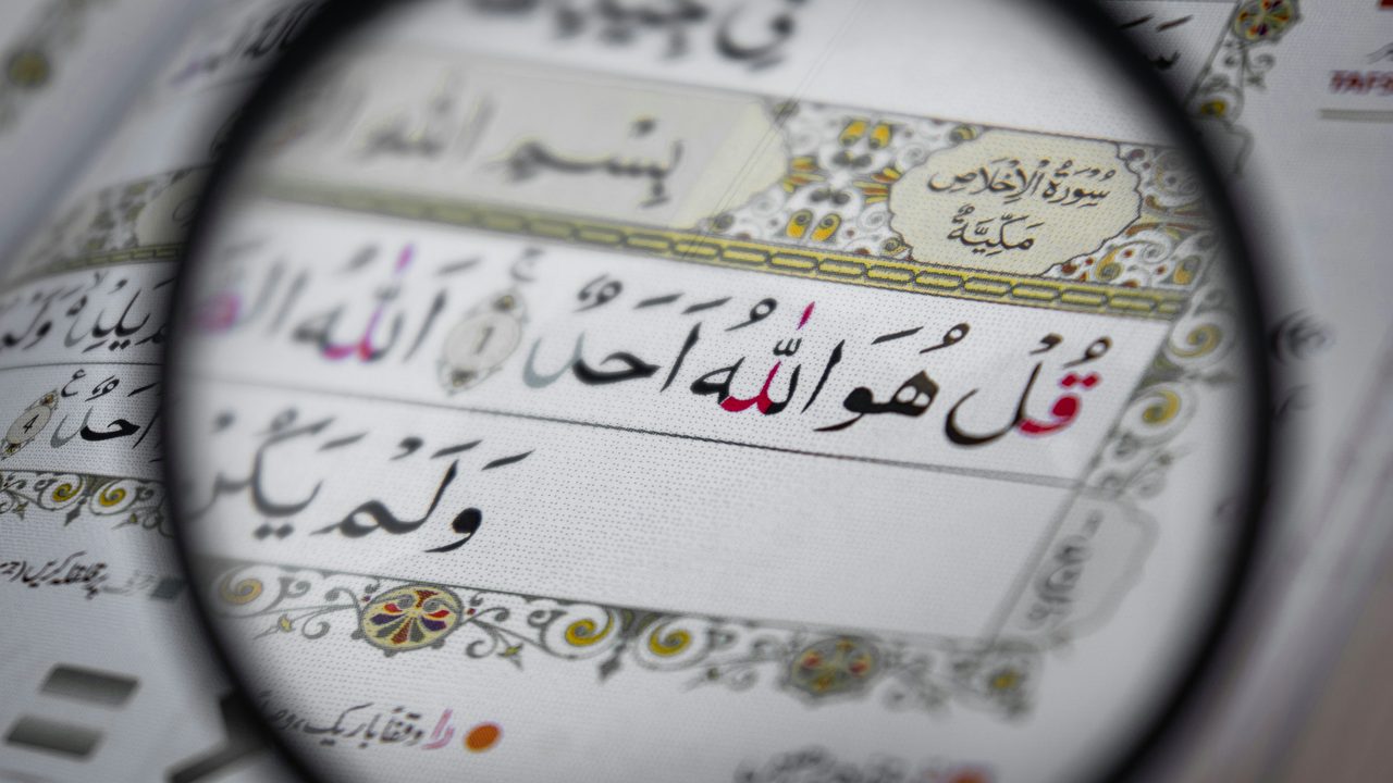 A magnifying glass held over the Arabic text of the Quran