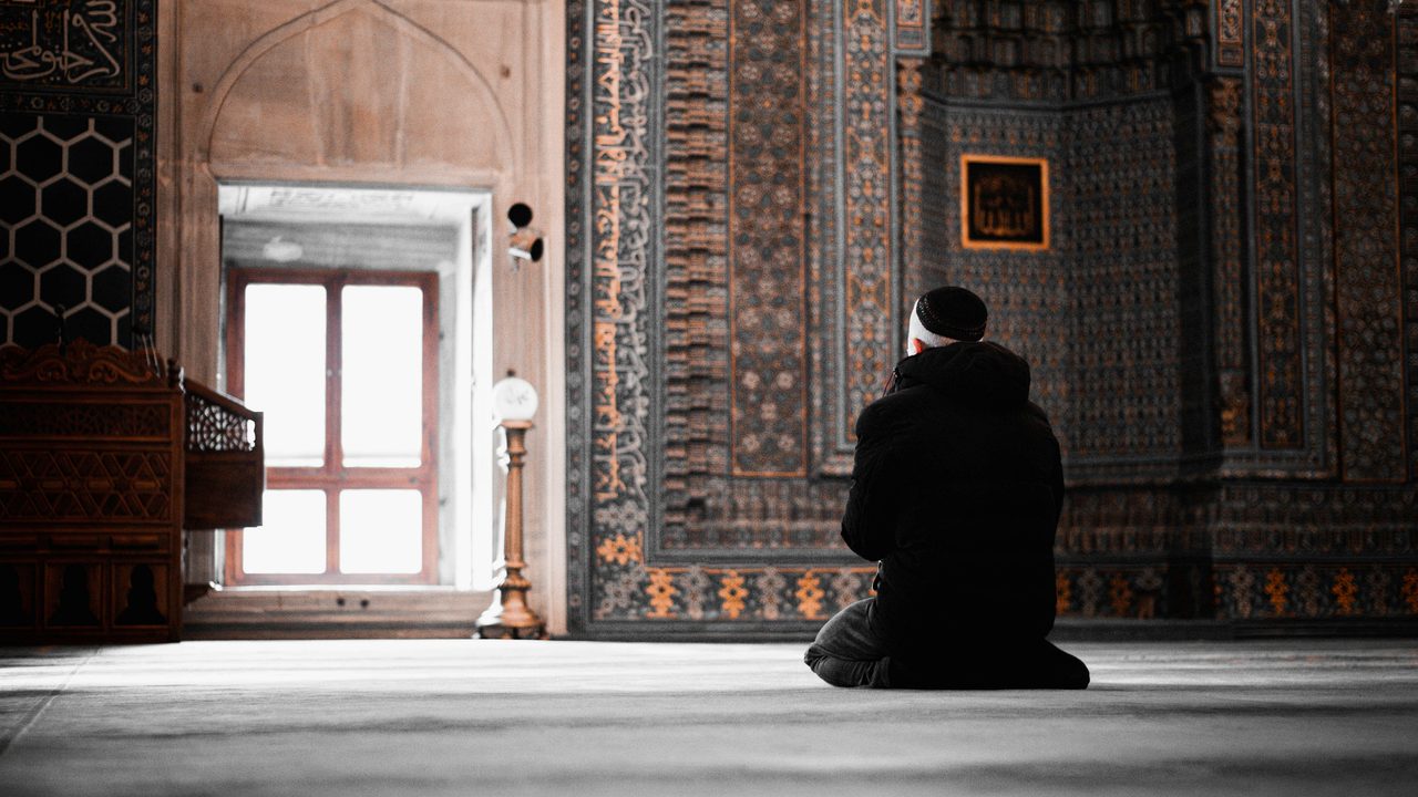 A man praying alone in a sunlit mosque