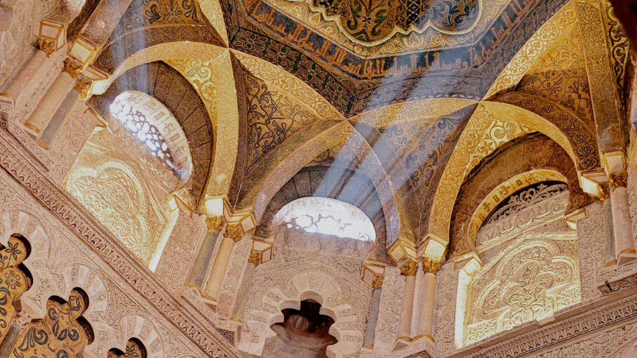 An ornate mosque ceiling lit by a beam of light