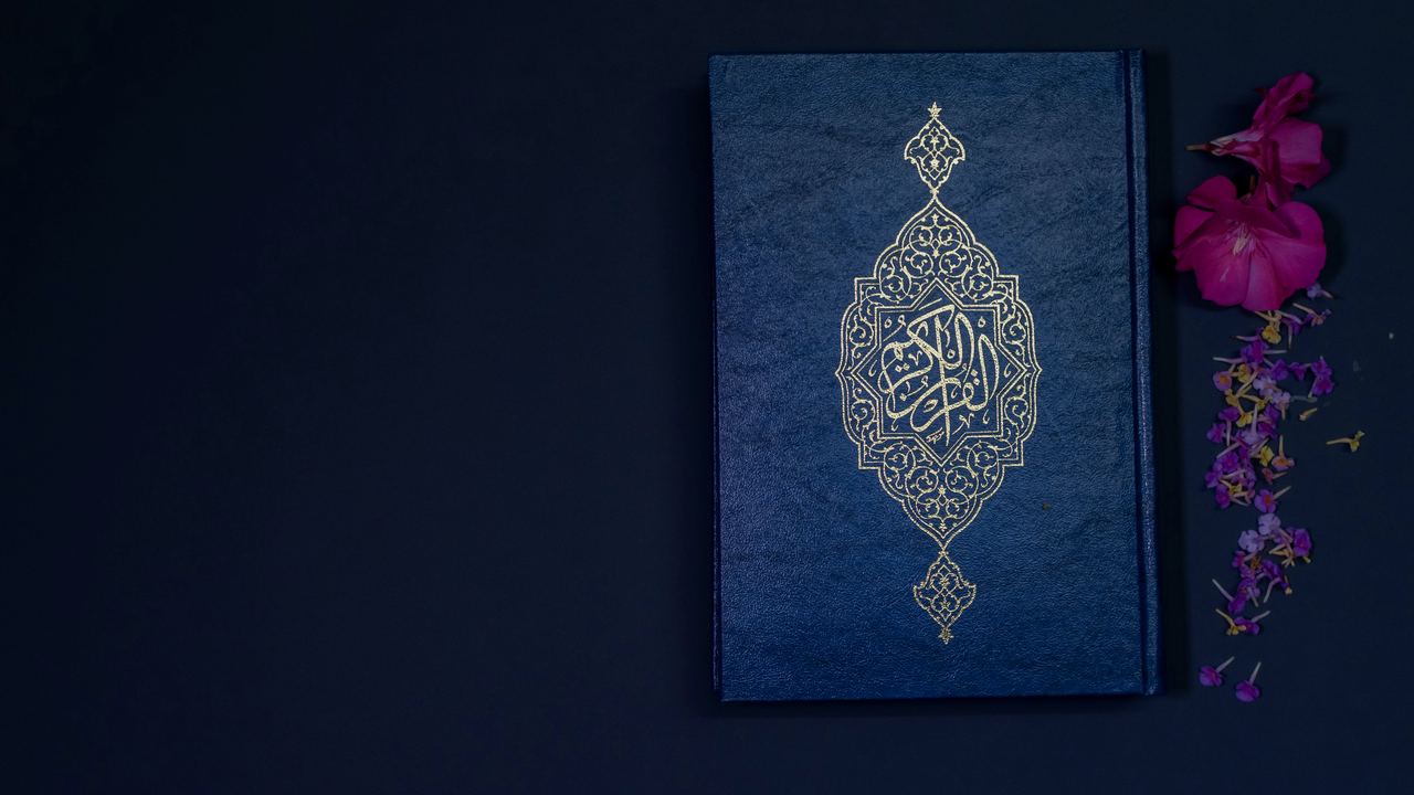 A Qur'an resting beside flowers on a dark surface